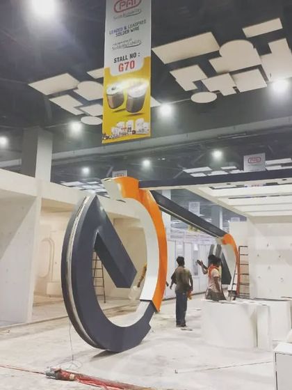 A wide shot of the Tinge booth during setup, showcasing its large, sculptural "G" element.