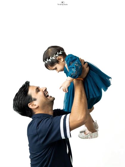 A father joyfully lifts his daughter in the air against a clean studio backdrop, a classic and heartwarming father-daughter photo.