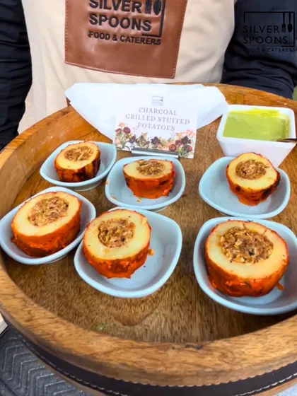 Charcoal Grilled Stuffed Potatoes served in individual dishes on a wooden tray. This appetizer offers a smoky flavor and a hearty filling, presented with a side of green chutney.