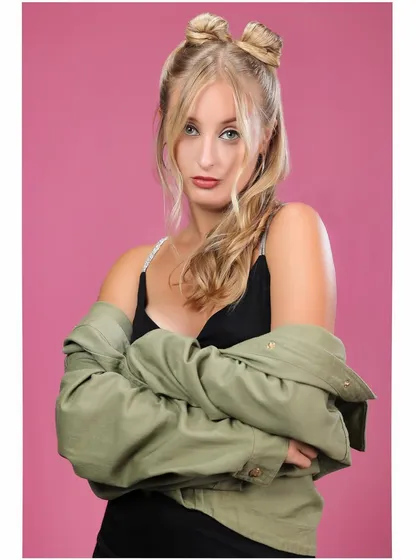 A stylish portrait of a model with space buns against a solid pink background.
