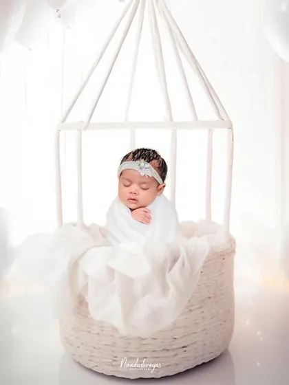 An all-white, dreamy setup to create a truly angelic portrait. Using soft textures, gentle lighting, and ethereal props like this birdcage basket, I craft a serene and timeless image of your sleeping newborn.