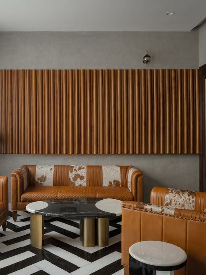 A bold and dramatic living area with a black-and-white chevron marble floor. The custom leather sofas and fluted wood wall paneling add texture and a touch of art deco glamour to the modern space.