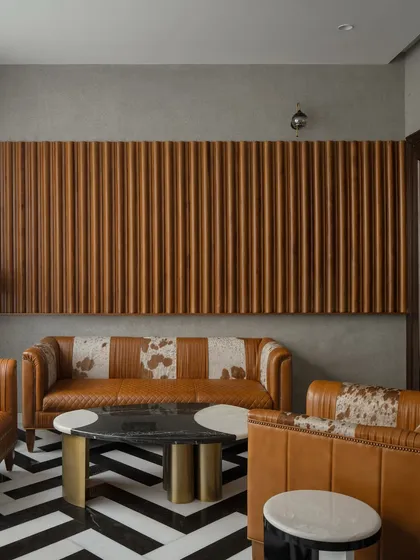 A bold and dramatic living area with a black-and-white chevron marble floor. The custom leather sofas and fluted wood wall paneling add texture and a touch of art deco glamour to the modern space.