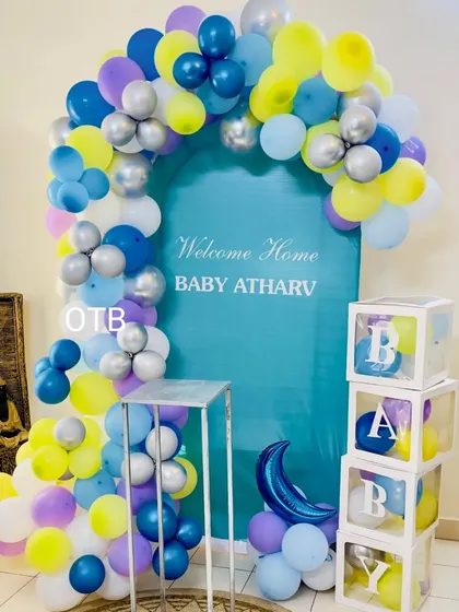 The completed welcome home setup for Baby Atharv. The arched backdrop is framed with a colorful balloon garland in pastel shades, and the "BABY" boxes add a popular, modern touch.