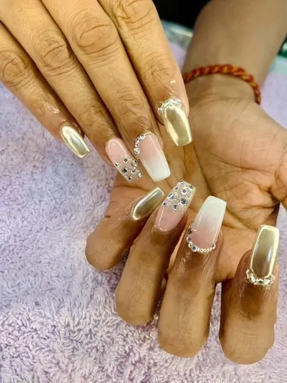 A glamorous set of long, square nails with a mix of gold chrome, ombre, and crystal-encrusted accent nails.