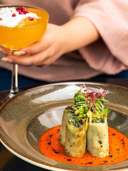 A beautifully plated dish of stuffed pasta rolls in a rich tomato sauce, paired with a creative cocktail. This is just one of the many flavorful dishes available on my Luncheon and Sundowner menu.