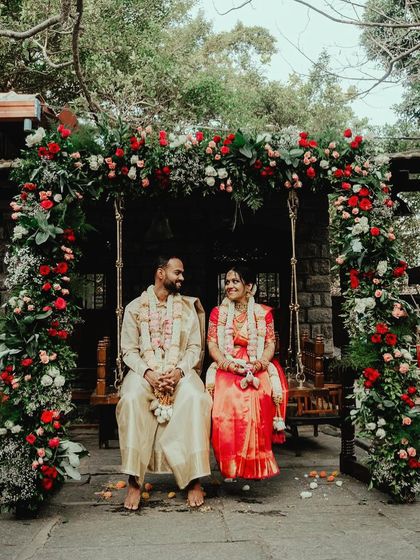 A couple sits on a floral-draped swing, framed by a beautiful arch of red and white roses.