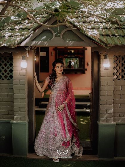 A portrait of the bride-to-be in her stunning pink lehenga, posing gracefully in a rustic, charming doorway.