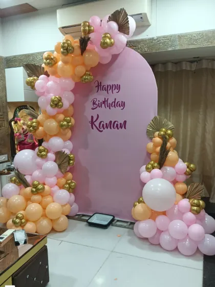 A warm and inviting birthday setup with a pink arched backdrop. The balloon garland in peach, pink, and gold tones adds a touch of elegance to this home decoration.