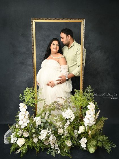 A creative portrait using a frame prop. The couple is captured within the golden frame, surrounded by white florals, creating a beautiful, artistic composition.