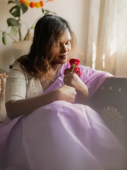 A tender moment captured indoors by a window. The model holds red roses, her expression soft and contemplative, as natural light fills the scene.