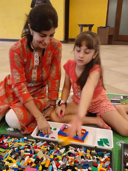 A mother helps her daughter sort through a tray of colorful LEGO bricks. It's a perfect example of the guided, supportive environment we foster in our sessions.