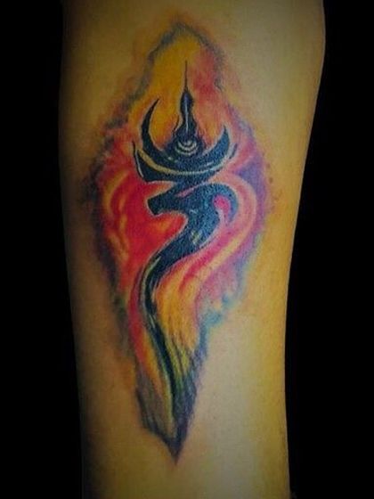 A vibrant, watercolor-style Om tattoo. The black Om symbol is surrounded by a fiery aura of yellow, red, and purple, giving it a dynamic and energetic feel. This is a great example of how we combine spiritual symbols with modern art styles.