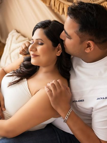 An intimate moment in the same boho setting. The partner gently kisses the mom-to-be's cheek as she closes her eyes, creating a peaceful and loving portrait.
