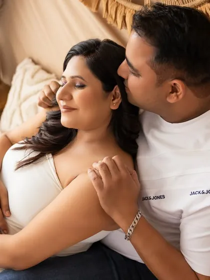 An intimate moment in the same boho setting. The partner gently kisses the mom-to-be's cheek as she closes her eyes, creating a peaceful and loving portrait.