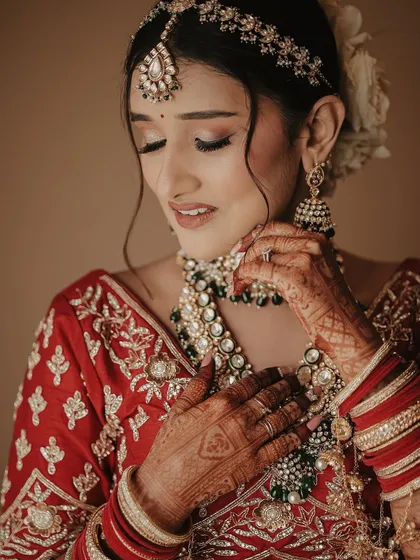 A close-up portrait focusing on the bride's serene expression and stunning jewelry. Her eyes are closed as she adjusts her necklace, a moment of calm before the ceremony.