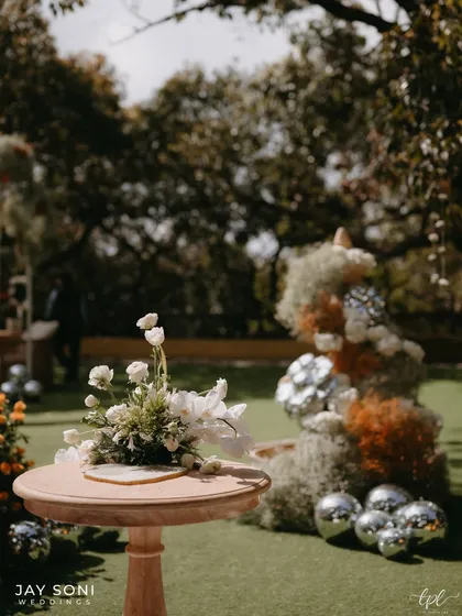 A detail shot from a vibrant wedding stage, showing a simple wooden table with a white floral arrangement, set against a backdrop of colorful blooms and disco balls.