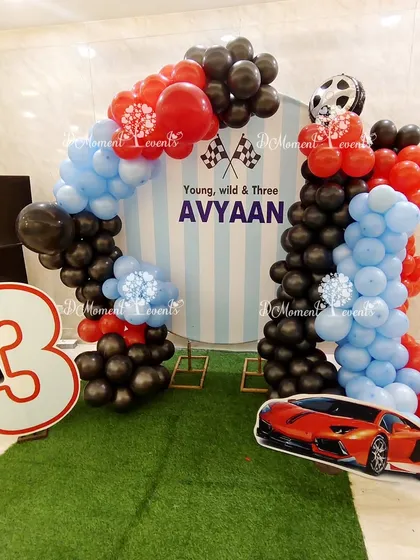 A cool and simple photo corner for a car-themed party, with a "Young, Wild & Three" backdrop, balloon arches, and a sports car cutout.