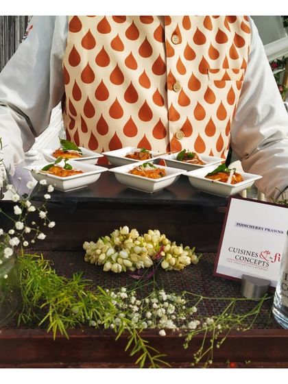 A tray of Jodhpuri Prawns, presented in individual white bowls and garnished with fresh herbs. The presentation on a bed of jasmine flowers adds a fragrant and beautiful touch to the service.