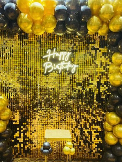 A classic and bold look with a gold shimmer wall framed by a black and gold balloon arch, perfect for any elegant birthday party.