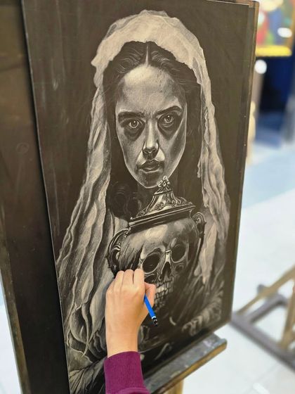 An over-the-shoulder view of the artist adding the final touches to her dramatic charcoal portrait, demonstrating her precise control of the medium.