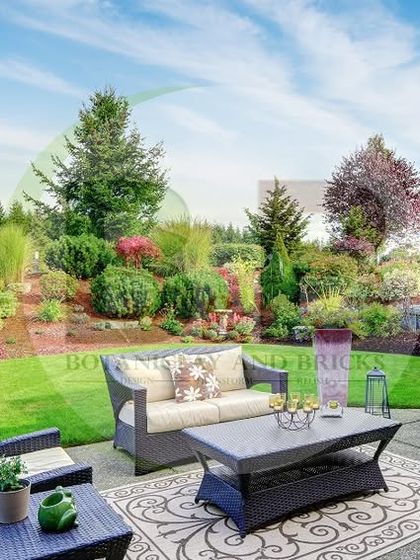 This spacious backyard combines a paved patio area for outdoor furniture with a large, open lawn surrounded by mature trees and shrubs. It's a perfect example of a functional family garden designed for both relaxation and recreation.