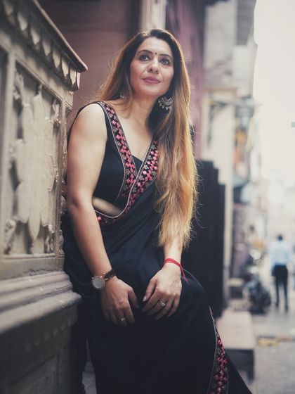 A beautiful portrait capturing the subject against the rustic walls of an old haveli. The soft light and her relaxed pose highlight the intricate border of the black saree.