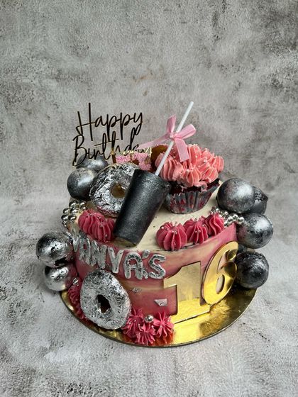 A sweet 16 deserves a fully loaded cake! This fun chocolate birthday cake is topped with donuts, a cupcake, and chocolates, all in a fun pink and silver color scheme.