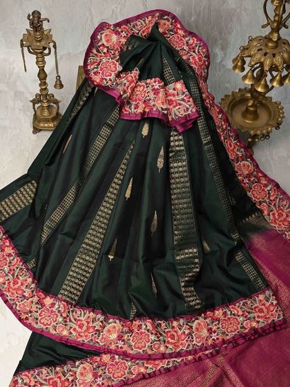 This dark green Kanjivaram silk saree features a stunningly detailed embroidered floral border in shades of pink and red. It’s a beautiful fusion of weaving and embroidery.