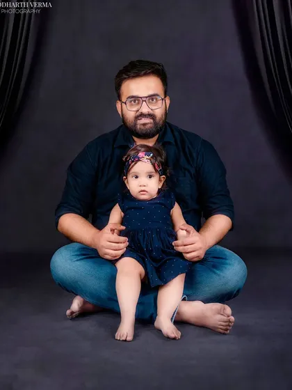 A father and his young daughter share a quiet moment. The dark background creates an intimate and focused portrait of their bond.
