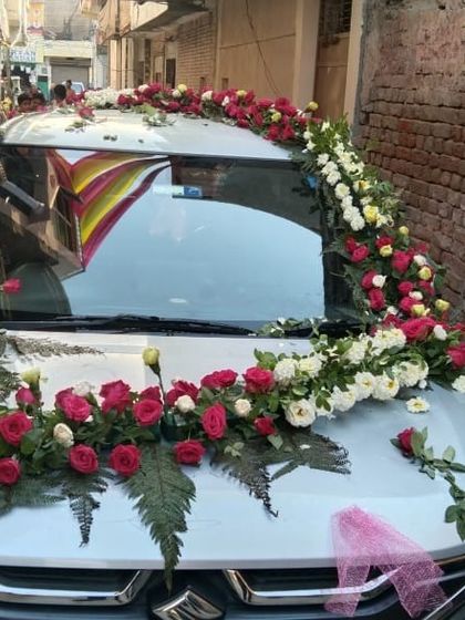 A floral arrangement of red and white roses with ferns on the bonnet of a silver car.