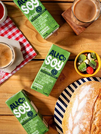 A cozy breakfast flatlay featuring Alt Co. Soy Drink. The overhead perspective, combined with a checkered napkin and fresh bread, creates a warm and inviting composition perfect for social media.
