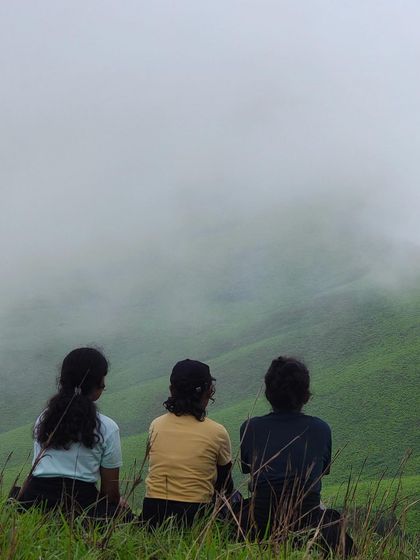 Three friends sitting together, looking out at the misty green valley from the Netravathi trail.