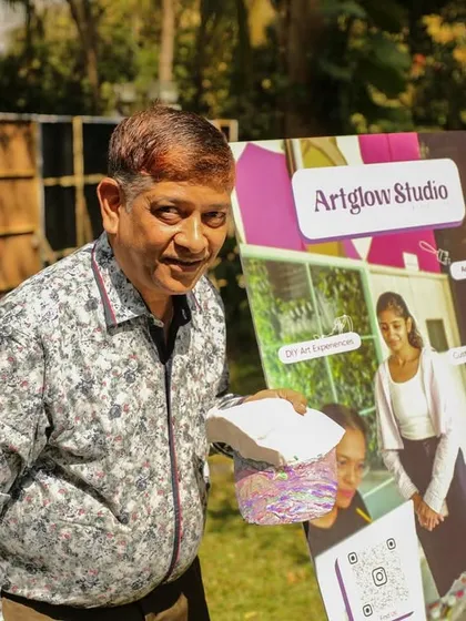 A happy guest at a wedding carnival, holding the cap he just painted next to my ArtGlow Studio sign.