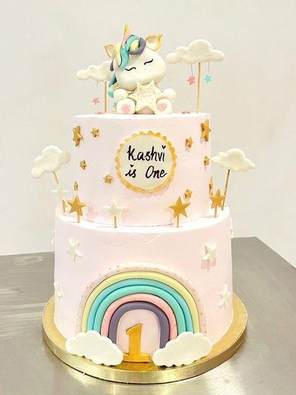 A magical two-tier unicorn cake for a first birthday. This cake is decorated with a rainbow, stars, clouds, and a sweet unicorn topper, creating a dreamy centerpiece for the celebration.