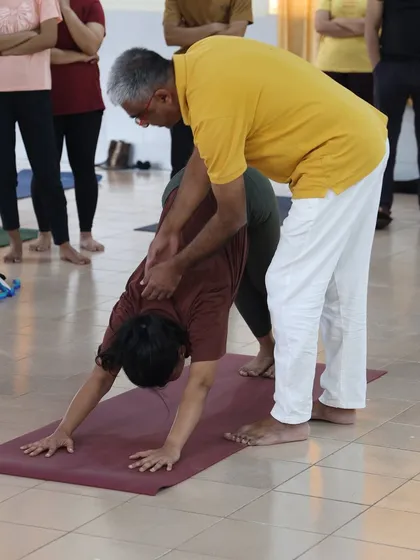 A teacher provides a correction in Adho Mukha Svanasana, the downward facing dog, a key posture in Surya Namaskar for stretching the entire body.