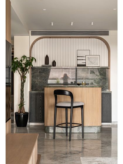 The arched bar area in the Noir Blanc House is a statement of elegance, with a sage green marble top, oak flutes, and black veneered cabinetry creating a harmonious blend of quiet luxury.