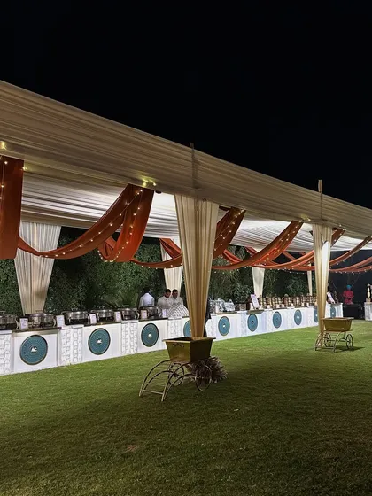 An elegant outdoor buffet setup under a tent, with rustic orange and cream drapes complemented by fairy lights.