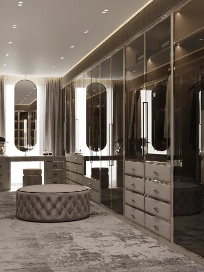 This closet design exudes a moody and sophisticated vibe with smoked glass doors and a dark color scheme. A plush, tufted ottoman sits at the center, providing a comfortable spot for dressing.