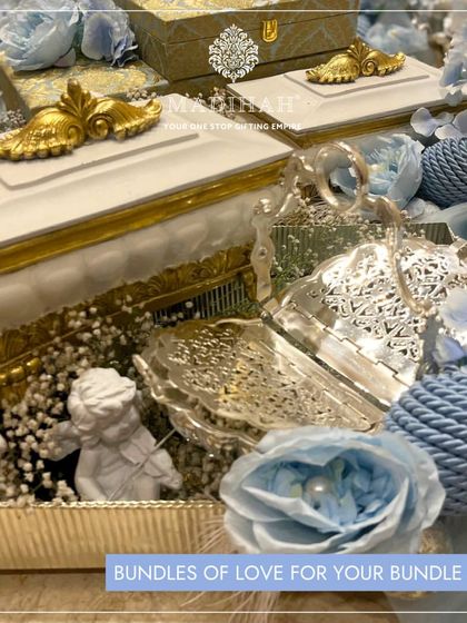 A beautiful arrangement for a baby boy, featuring a silver-plated filigree dish and a white keepsake box with gold trim. The hamper is surrounded by blue flowers, perfectly capturing 'Bundles of love for your bundle of joy'.