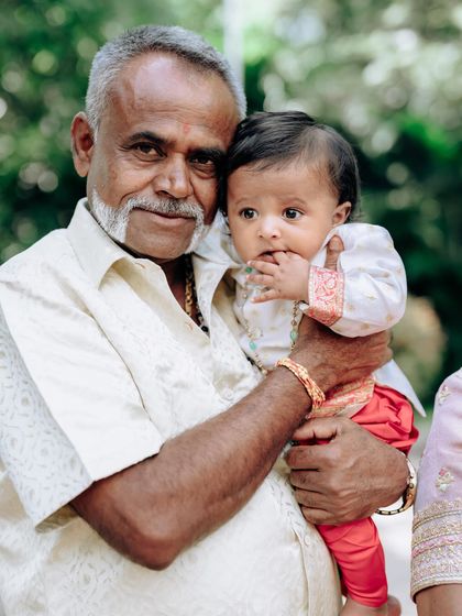 A grandfather holds his grandson, both looking dapper. It's a joy to design for multiple generations, creating outfits that connect family members through style.