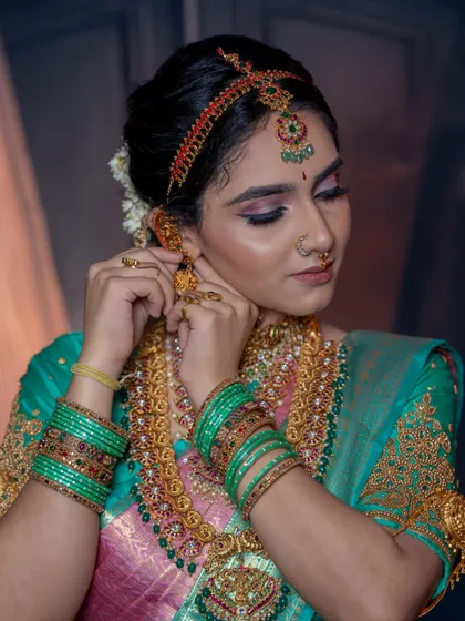 A close-up showing the model adjusting her earrings, highlighting the detailed eye makeup and jewellery.