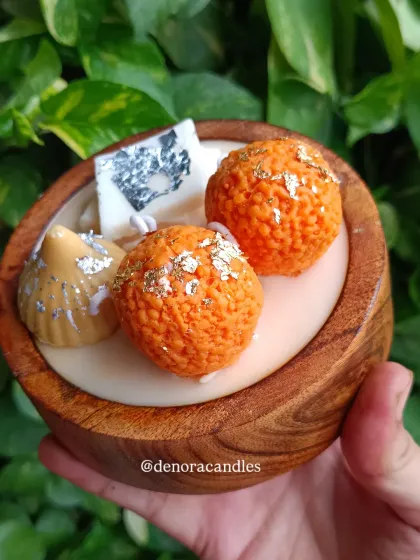 A close-up of the dessert platter candle, focusing on the gold and silver leaf details on the laddoo and modak.