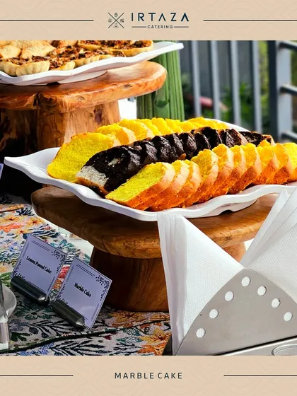 A close-up of the Lemon Pound Cake and Marble Cake from a daytime event. The beautiful patterned tablecloth and simple labels add to the charming presentation.