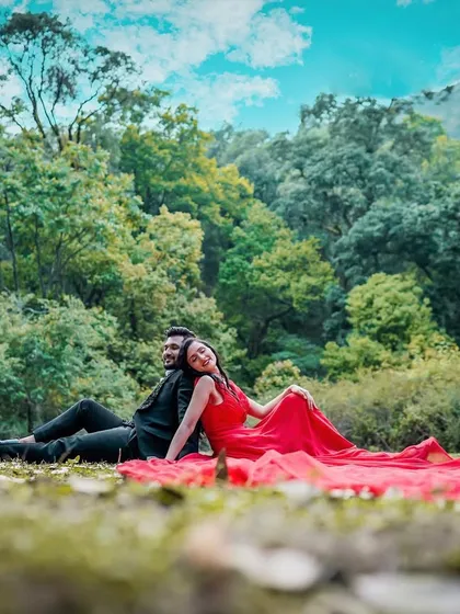 A relaxed and romantic moment from a couple's pre-wedding shoot. This image captures the couple sitting together in a natural setting, showcasing their connection against a lush forest backdrop.
