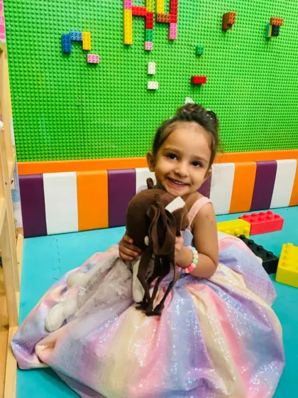 A little princess takes a break from building with giant Lego blocks to give a happy smile.