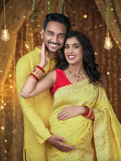 A joyful couple's portrait with a festive background of hanging lights and marigolds, perfect for celebrating the upcoming arrival.