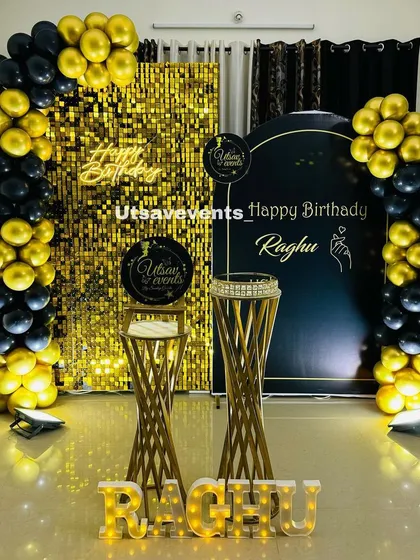 A sophisticated black and gold themed decoration for a birthday celebration. The design combines a gold shimmer wall with a sleek black backdrop and matching balloon arches for a truly glamorous look.