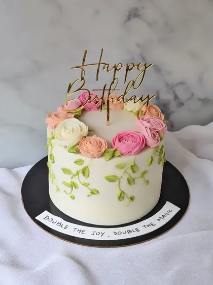 A floral beauty for a double birthday celebration. This cake features a wreath of hand-piped buttercream flowers in shades of pink and peach.