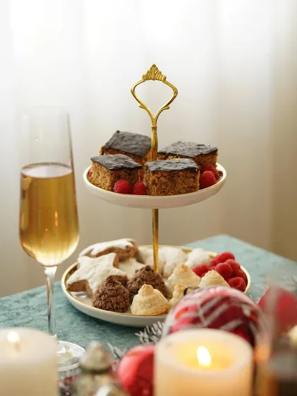 A tiered stand of Christmas cakes and cookies, styled with champagne and candles for an elegant holiday feel.